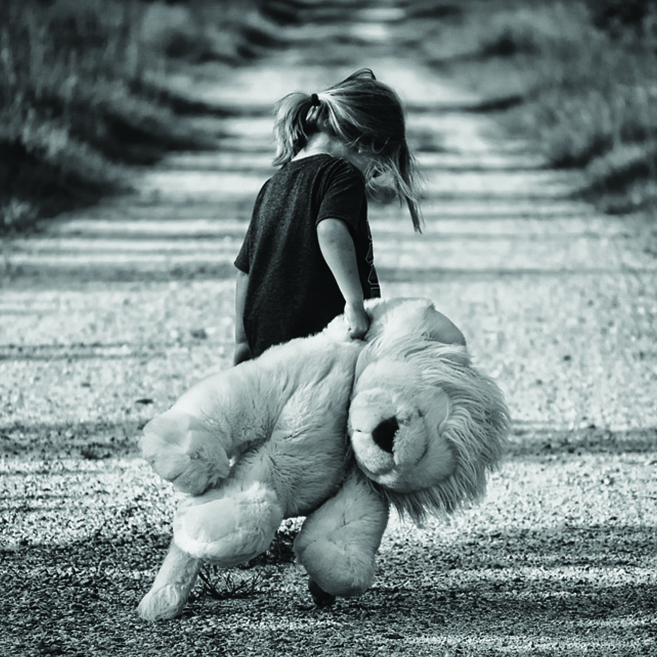 Black-and-white photo of a young girl dragging a stuffed lion down a long gravel road, symbolizing the journey of leaving behind trauma.