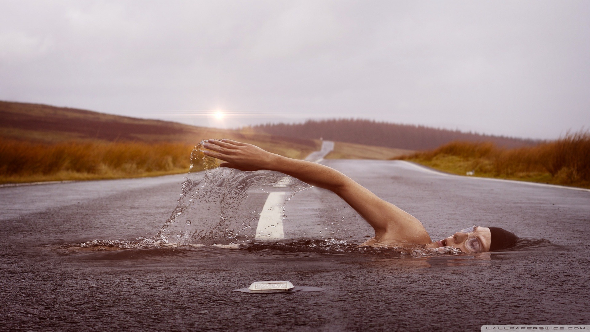 Man swimming across an asphalt road with the long road behind him. The image symbolizes getting through a rough patch in one's life's journey.