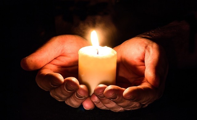 Two hands holding a lit candle against a dark background, symbolizing hope, safety, and confidentiality in the evaluation process.