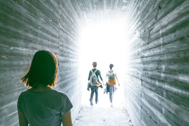 Silhouette of two people walking into a bright white light at the end of a tunnel, symbolizing a clear path and hope for the future.